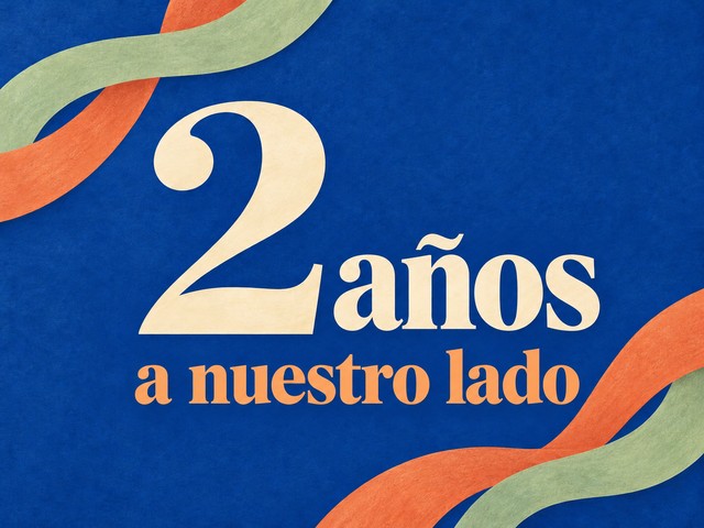 Ilustración de letras crema y albaricoque con cintas de colores sobre azul cobalto, con el mensaje «2 años a nuestro lado»