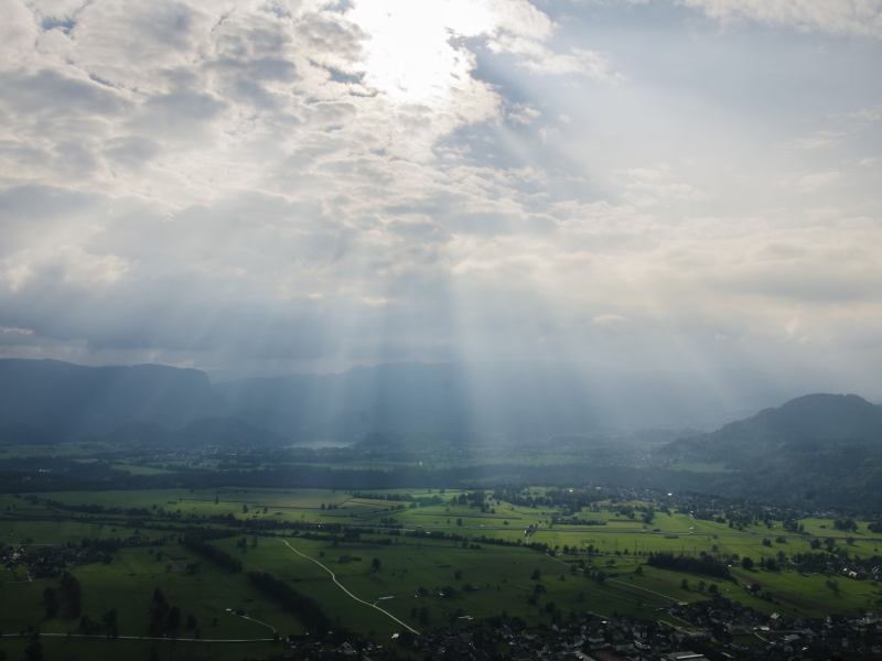 Paisaje con colinas bajo un cielo nublado, con rayos de sol atravesando las nubes.